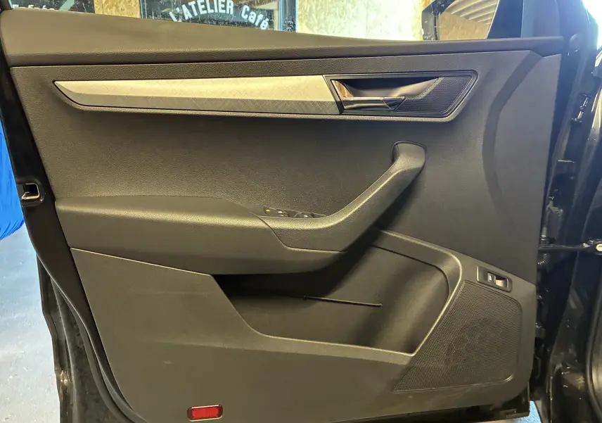 Porte intérieure côté gauche noire du Skoda Karoq 2024 avec poignée chromée et haut-parleur intégré.