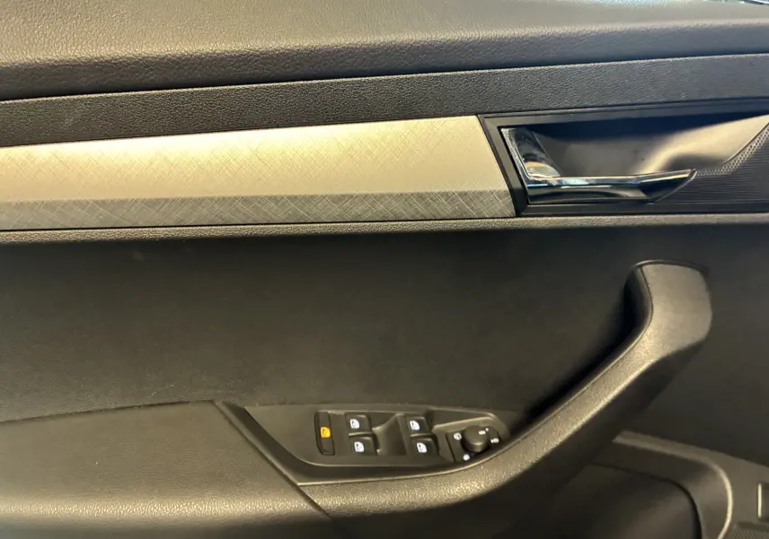 Détail de la porte côté gauche du Skoda Karoq noir 2024 avec poignée intérieure chromée et commandes de vitres électriques.