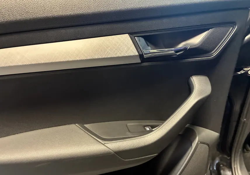 Détail de la porte intérieure droite noire du Skoda Karoq 2.0 TDI 116 DSG7 Business avec poignée chromée et insert décoratif argenté.