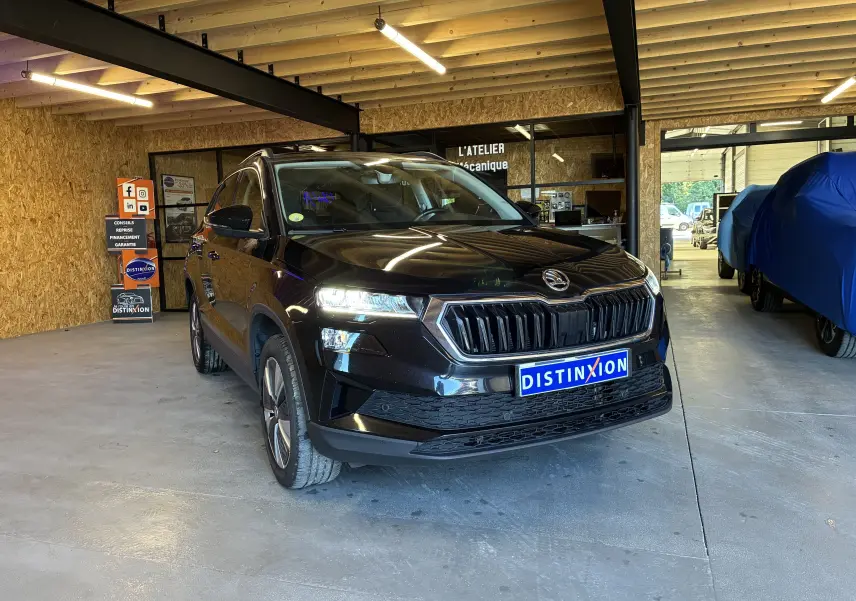 Vue 3/4 avant d'un Skoda Karoq noir 2024 avec calandre noire chromée et jantes alliage 17'' dans un garage.