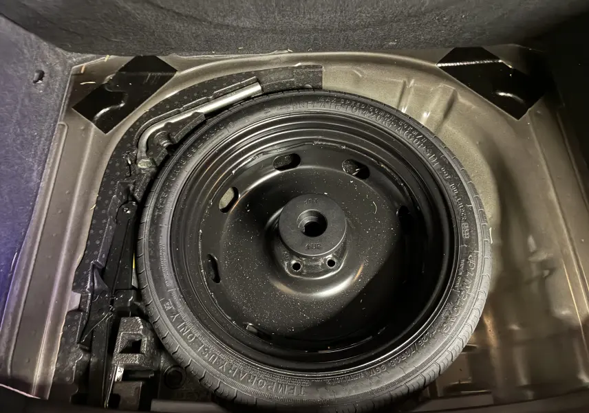 Roue de secours galette noire vue de dessus dans le coffre d'un Skoda Karoq 2024, avec outils de changement.