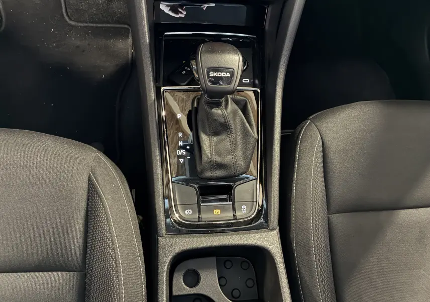 Vue plongeante sur la console centrale noire du Skoda Karoq 2024 avec levier de vitesses DSG et sièges tissu gris.