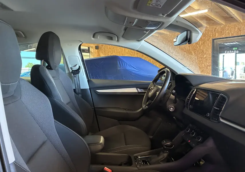 Vue intérieure côté conducteur du Skoda Karoq 2024 noir, avec sièges tissu noirs et tableau de bord moderne.