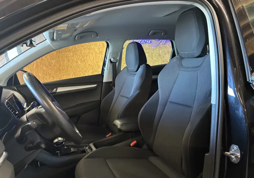 Vue intérieure côté conducteur du Skoda Karoq noir 2024, sièges tissu noir avec coutures contrastées et tableau de bord moderne.
