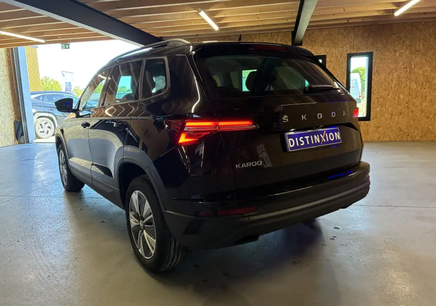Vue 3/4 arrière droite du Skoda Karoq noir 2024 avec feux arrière LED allumés dans un garage.