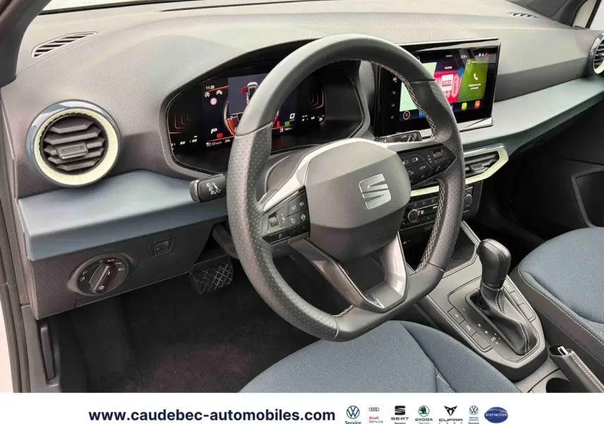 Vue intérieure côté conducteur du SEAT Arona blanc 2026, volant cuir multifonction et écran tactile central visible.