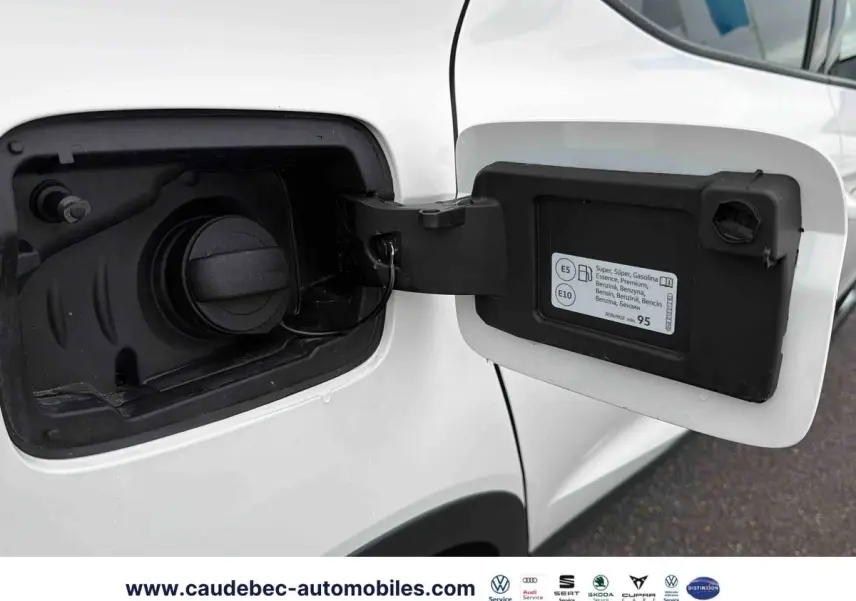 Vue rapprochée de la trappe à carburant ouverte côté gauche d’une SEAT Arona blanche, avec bouchon essence visible.