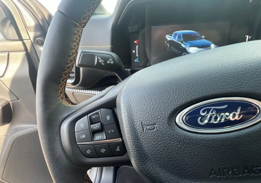 Vue rapprochée du volant cuir noir avec surpiqûres orange et tableau de bord digital du Ford Ranger gris carbone 2025.