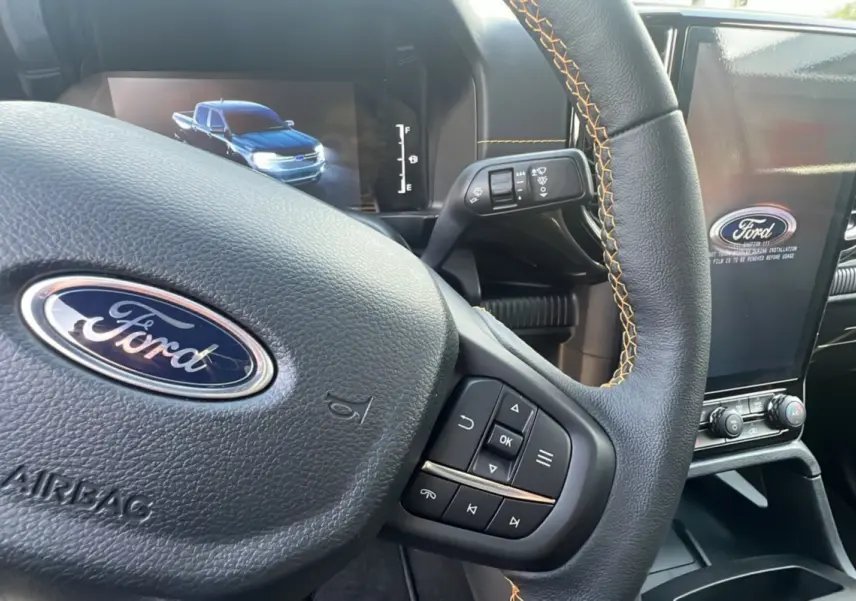 Gros plan sur le volant en cuir noir avec surpiqûres orange du Ford Ranger Wildtrak 2025 et écran central tactile.