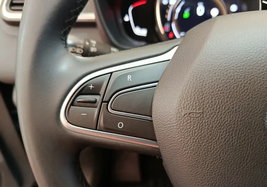 Gros plan sur les commandes du volant noir du Renault Kadjar Business gris foncé, avec tableau de bord lumineux en arrière-plan.