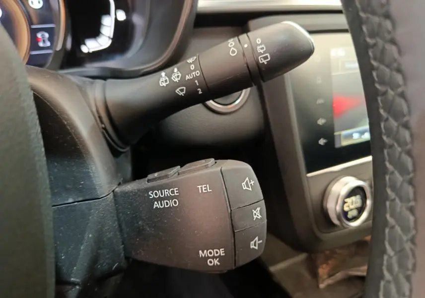Gros plan sur la commande audio au volant d'un Renault Kadjar gris foncé, avec tableau de bord et écran tactile en arrière-plan.