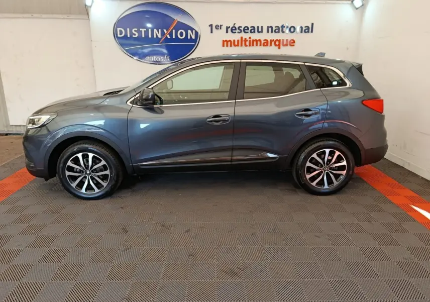 Profil latéral droit d'un Renault Kadjar Business gris foncé, avec jantes alliage et rails de toit chromés visibles.