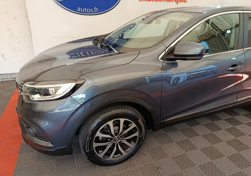 Vue 3/4 avant droit du Renault Kadjar Business gris foncé avec jantes alliage et feux LED visibles en intérieur showroom.