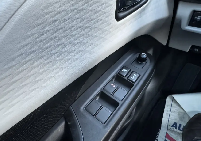 Gros plan sur les commandes de lève-vitres et réglage des rétroviseurs côté conducteur d'une Suzuki Swift blanche 2025.