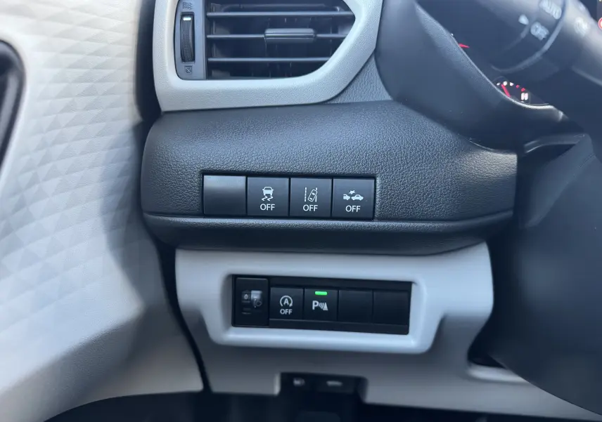 Vue rapprochée des commandes noires sur tableau de bord gris clair côté gauche du Suzuki Swift blanc hybride 2025.
