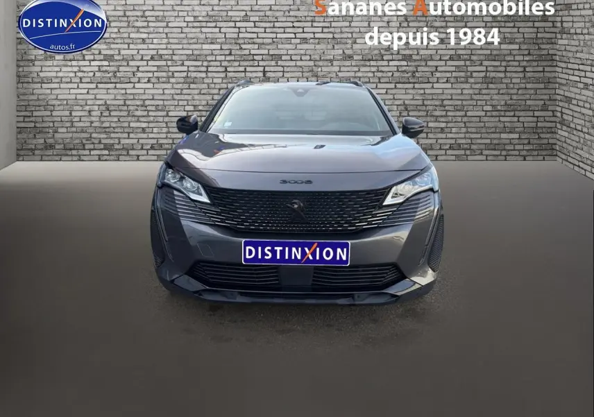 Vue avant d'un Peugeot 3008 gris foncé avec calandre noire et logo lion Dark Chrome sur fond urbain en briques.