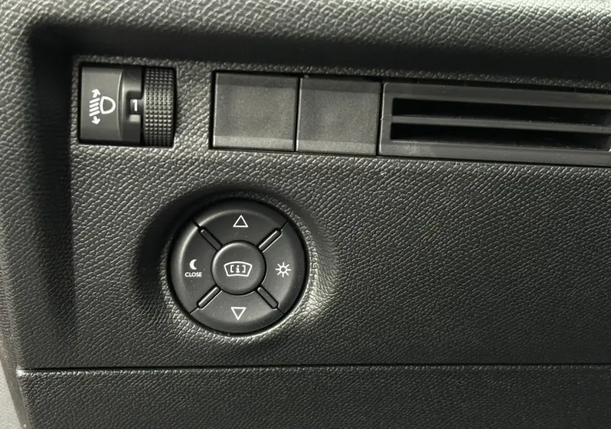 Détail du tableau de bord noir texturé avec commandes de réglage des phares et de l'affichage dans une Citroën C4 Hybrid 2025.