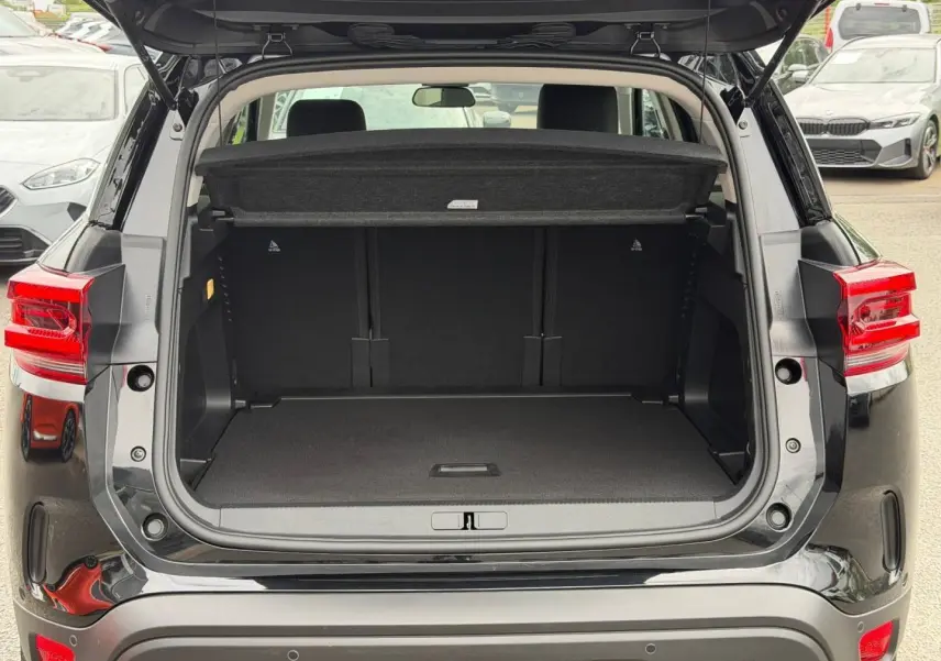 Coffre ouvert vu de l’arrière d’un Citroën C5 Aircross noir Perla Nera avec cache-bagages et feux arrière LED visibles.