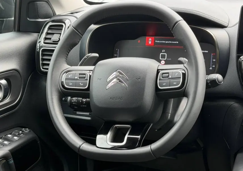 Vue rapprochée du volant cuir multifonction noir du Citroën C5 Aircross 2025 avec tableau de bord numérique allumé.