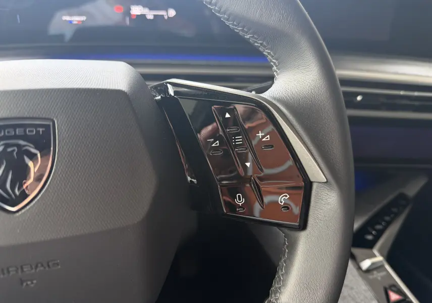 Gros plan sur les commandes à droite du volant noir du Peugeot 1007, avec logo lion et tableau de bord en arrière-plan.
