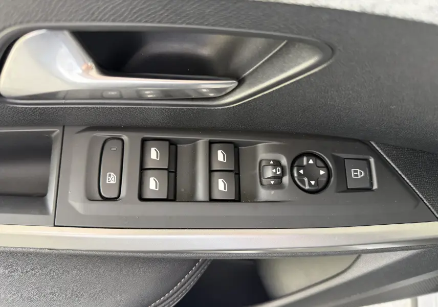 Gros plan sur la commande des vitres et rétroviseurs côté gauche d’une Peugeot 1007 gris Artense, intérieur noir.