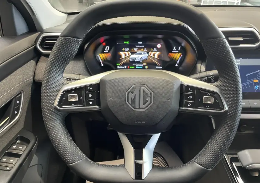 Vue rapprochée du volant en cuir perforé et du tableau de bord numérique du MG Motor ZS 1.5 Hybrid+ gris clair 2026.