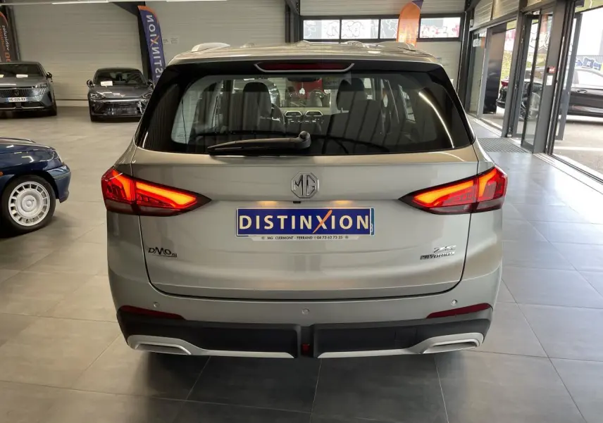 Vue arrière d’un MG ZS 1.5 Hybrid+ gris clair avec feux arrière LED allumés en showroom.