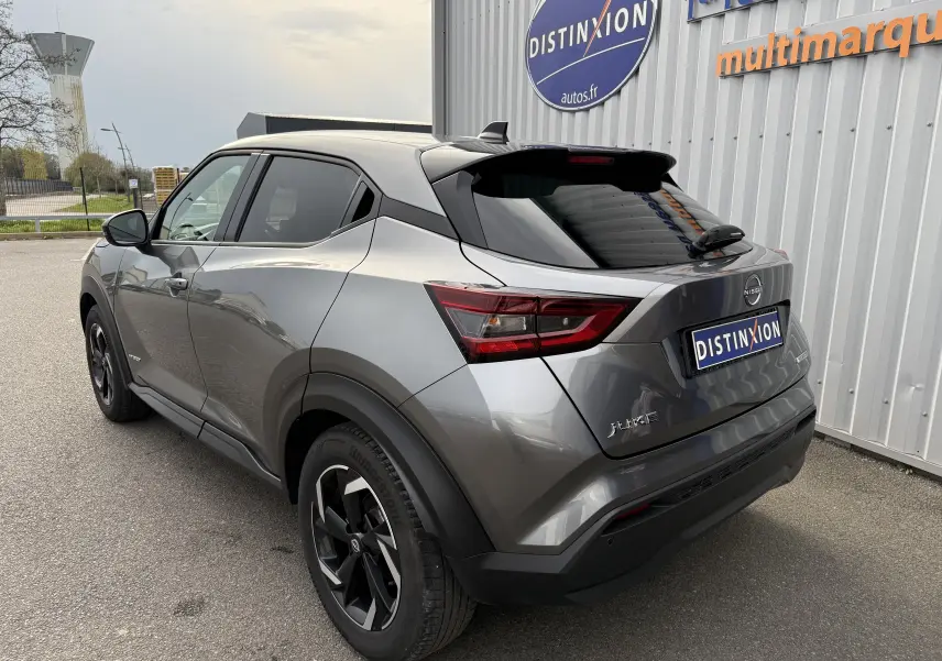 Nissan Juke 2024 gris squale métal vu en 3/4 arrière droit, avec toit noir et jantes bi-ton distinctives.