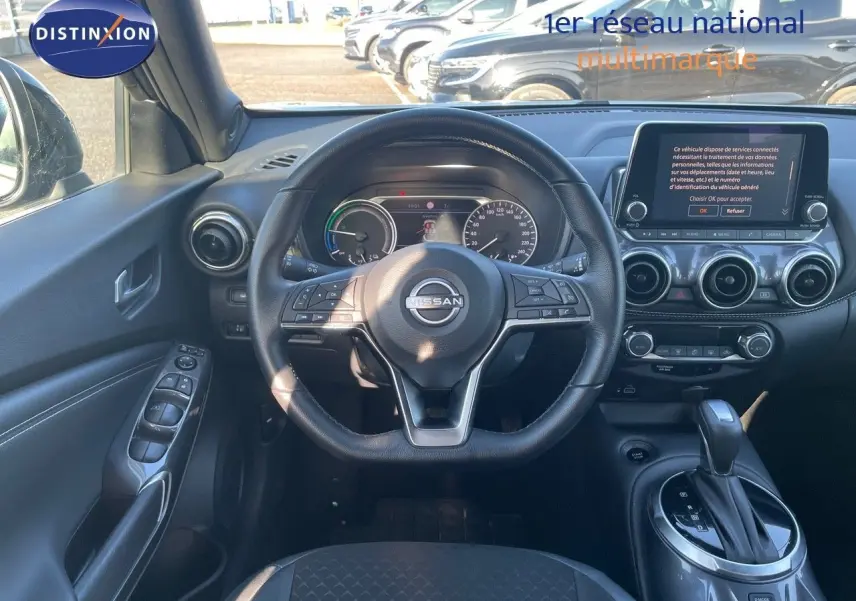 Vue intérieure du poste de conduite du Nissan Juke 2024 gris, avec volant multifonction et écran tactile central.