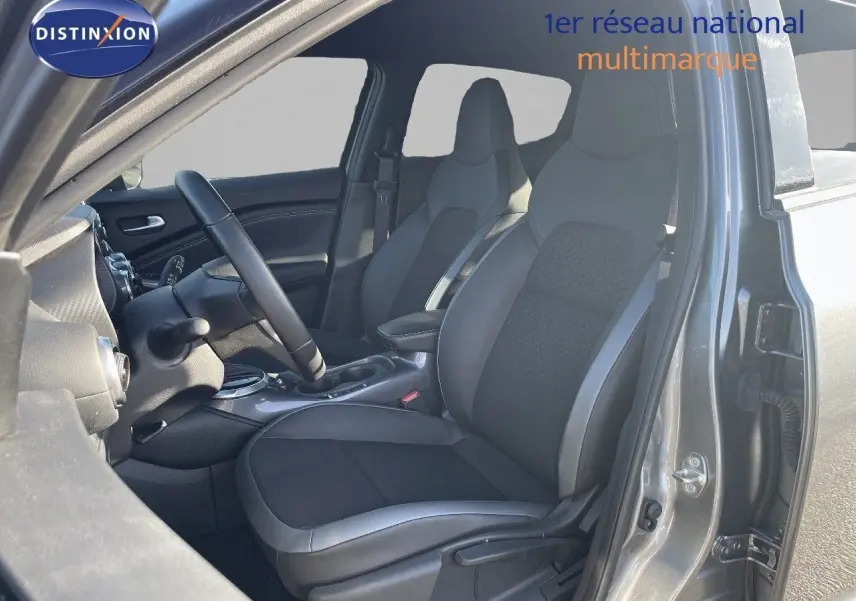 Intérieur avant droit du Nissan Juke gris squale métal 2024, sièges en cuir gris et tissu avec console centrale visible.