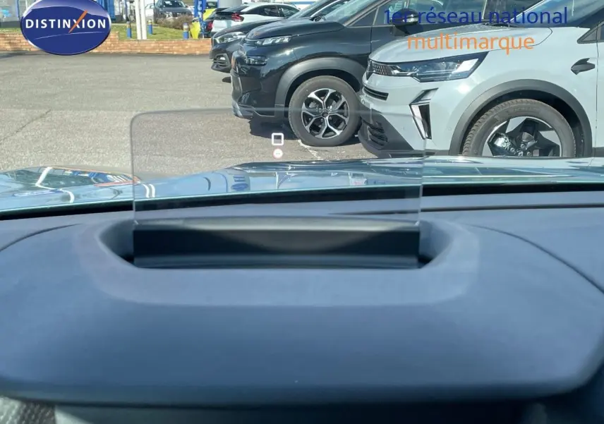 Vue depuis l'intérieur sur le tableau de bord et le pare-brise, avec plusieurs SUV gris et noir en stationnement devant.