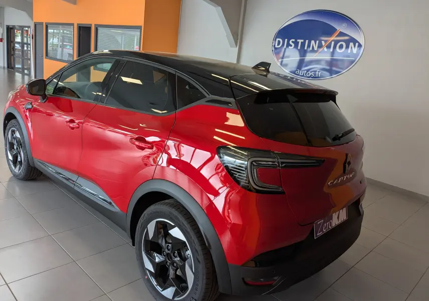 Vue 3/4 arrière droite du Renault Captur 2025 rouge flamme avec toit noir et jantes alliage noires en showroom.