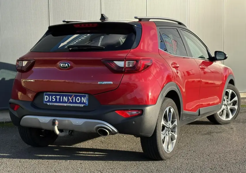 Vue 3/4 arrière droite d'un KIA Stonic rouge métallisé avec attelage et jantes alliage 17 pouces, vitres arrière surteintées.