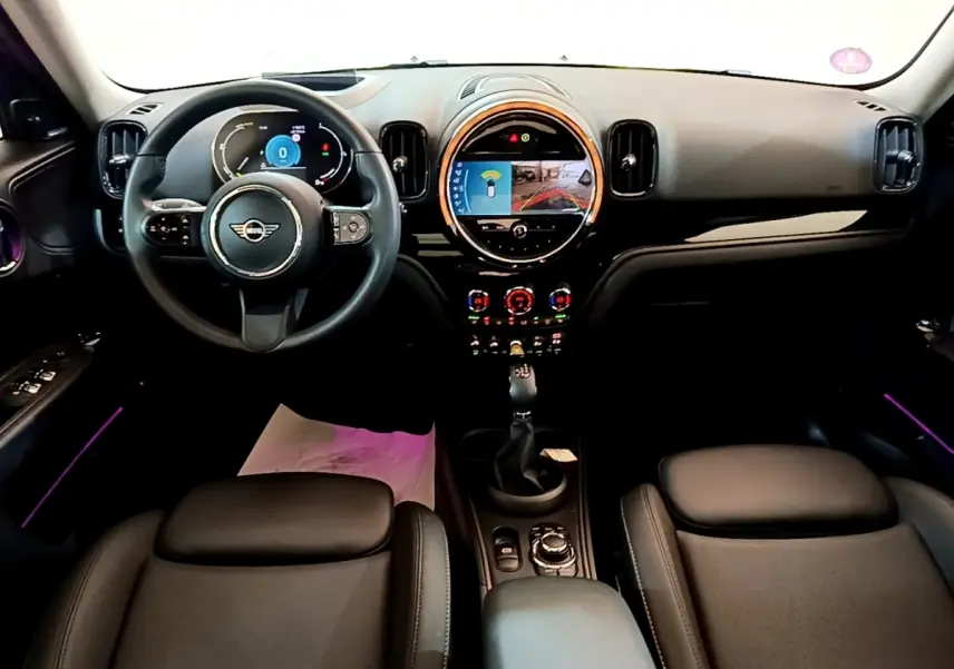 Vue intérieure frontale du tableau de bord et volant cuir noir du MINI COUNTRYMAN Cooper SE 2023 avec écran tactile central rond.