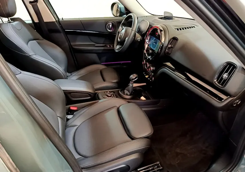 Intérieur avant droit du MINI Countryman vert 2023, sièges cuir noirs et tableau de bord avec écran tactile rond lumineux.