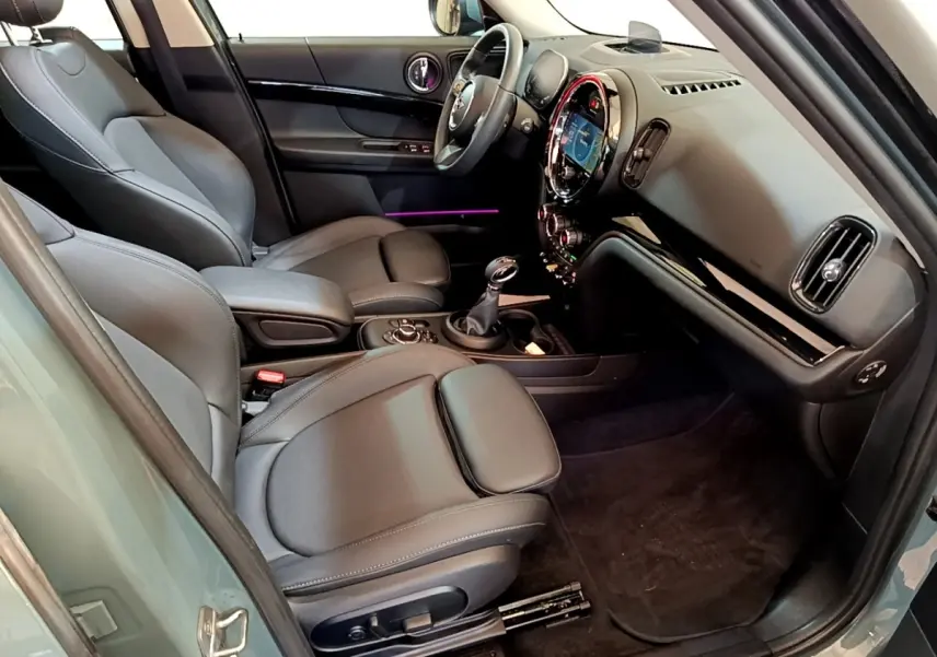 Intérieur avant droit du MINI Countryman vert 2023, sièges cuir noirs et tableau de bord avec écran tactile rond lumineux.