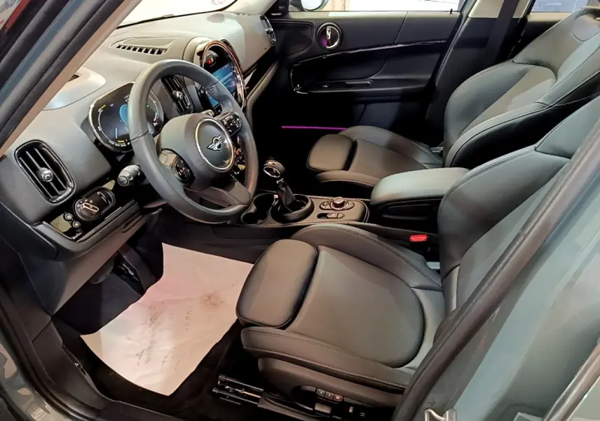 Intérieur avant droit du MINI Countryman vert 2023, sièges cuir noirs et tableau de bord avec écran tactile lumineux.