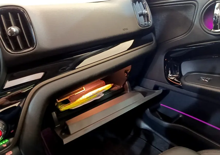 Intérieur MINI Countryman Cooper SE 2023, vue du côté passager avec boîte à gants ouverte et éclairage d’ambiance violet.