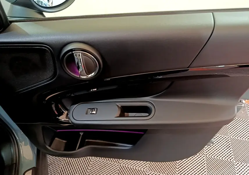 Vue rapprochée de la porte côté gauche du MINI Countryman vert avec éclairage d'ambiance violet et commandes électriques.
