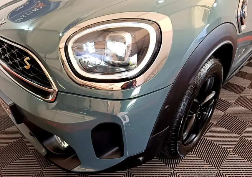 Gros plan sur le phare avant gauche et la roue noire d'une MINI Countryman Cooper SE vert métallisé.