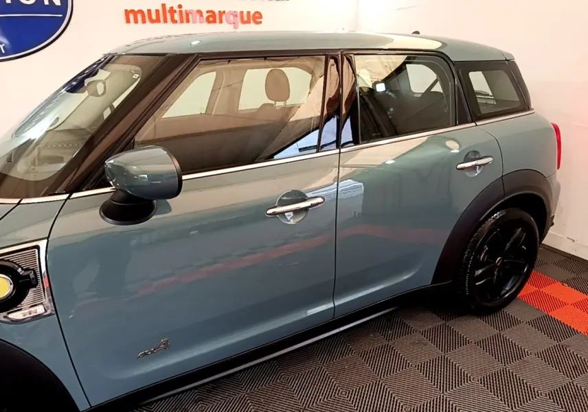 Vue latérale côté gauche d'un MINI Countryman hybride rechargeable vert avec toit blanc et jantes noires.