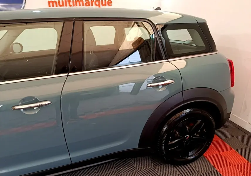 Vue côté droit arrière d'une MINI Countryman hybride rechargeable verte avec jantes noires brillantes et poignées chromées.