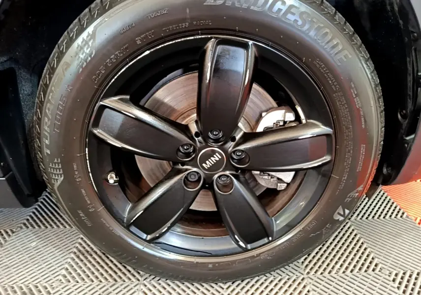 Gros plan sur la jante noire à cinq branches avec logo MINI au centre, montée sur un pneu Bridgestone.