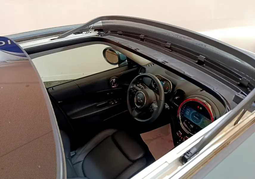 Vue intérieure du tableau de bord et volant cuir noir d'une MINI Countryman hybride rechargeable 2023, toit ouvrant ouvert.