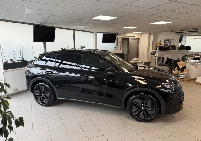 Vue de profil côté gauche d’un Volkswagen T-Roc noir intense en version Black R-Line, intérieur et jantes noires, en showroom.