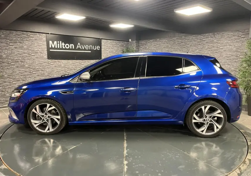 Profil droit d’une Renault Mégane GT bleu Iron 2016 avec jantes alliage 18 pouces et vitres surteintées.
