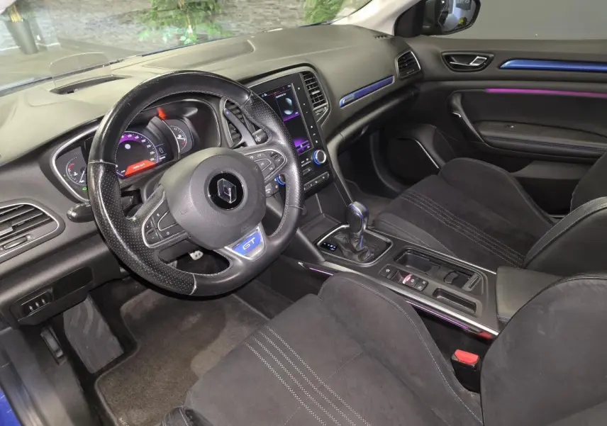 Vue intérieure côté conducteur de la Renault Mégane GT 2016 avec sellerie noire, volant GT et éclairage d’ambiance violet.