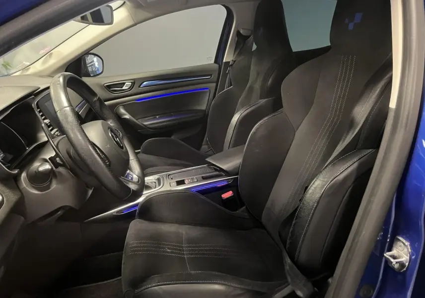Vue intérieure côté conducteur de la Renault Mégane GT 2016 avec sièges sport noirs et éclairage d’ambiance bleu.