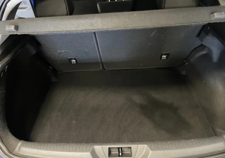 Vue plongeante sur le coffre vide de la Renault Mégane GT bleu, montrant la banquette arrière rabattable et le tapis noir.