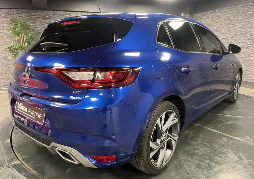 Vue 3/4 arrière droite d'une Renault Mégane GT bleue Iron avec jantes alliage 18 pouces et vitres surteintées.